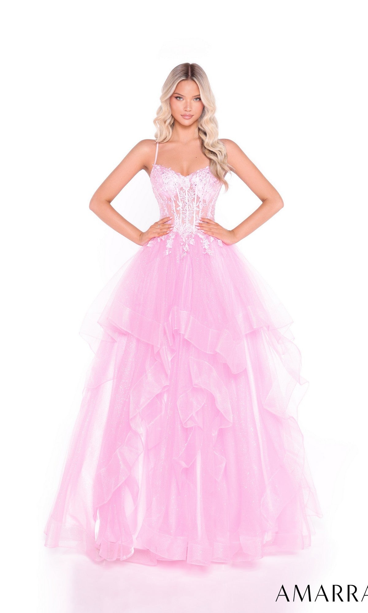 A woman poses against a white background wearing the Amarra 89504: a light pink, lace-up, long tiered prom dress with spaghetti straps and a fitted, embellished bodice.